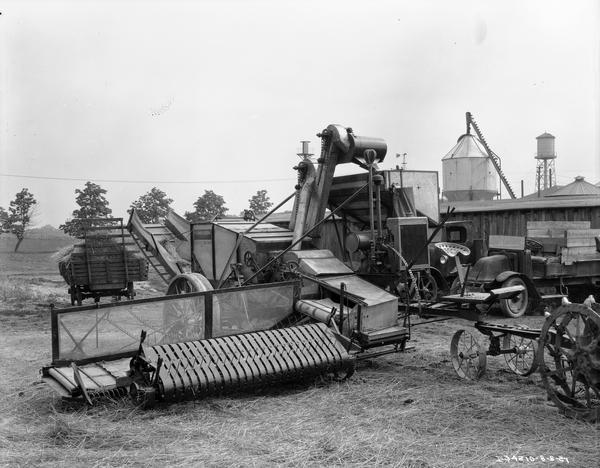 Farm machinery stored in a farm yard, including a No. 8 harvester-thresher, a wagon, and two International trucks.