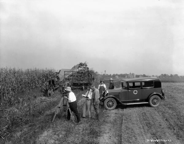 Camera crew from the Cloud County Farm Bureau filming farmers harvesting corn with a Farmall tractor. An International truck used by the crew is parked to the right.