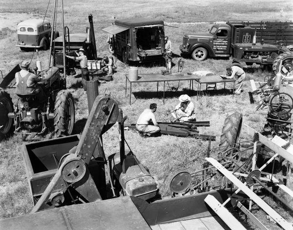 Elevated view of men sitting and working among Farmall tractors, combines (harvester-threshers) and trucks, possibly outside an International Harvester dealership.
