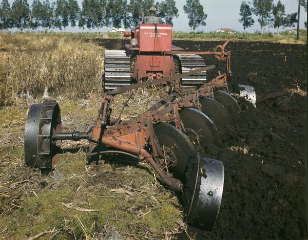 Rear view of an African American man plowing a field with an International diesel crawler tractor (TracTracTor) and a disk plow.