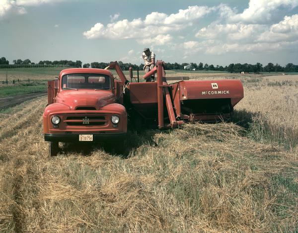 Man working in a field with an International truck and a McCormick harvester-thresher (combine).