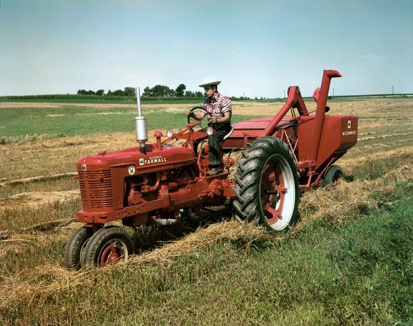 Three-quarter view from front left side of a man pulling a combine (harvester-thresher) in a field with a Farmall Super H tractor.