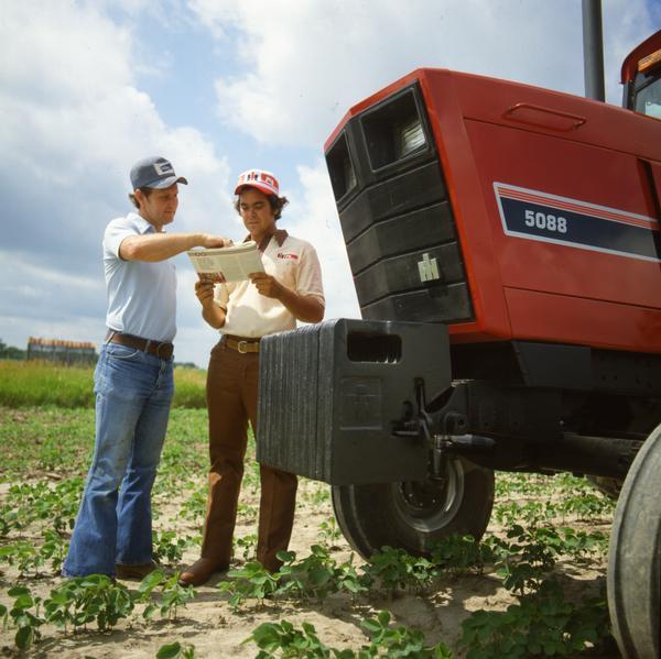 Color photograph of two men having a conversation next to an International 5088 tractor.