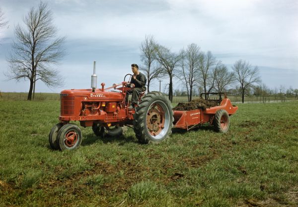 Man pulling a manure spreader with a McCormick Farmall H tractor.