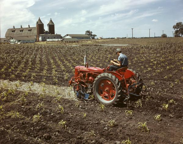 View towards a man in a field operating a McCormick C Tractor with a front-mounted cultivator. The color photograph was taken either at or near the company's experimental farm in Hinsdale, Illinois.