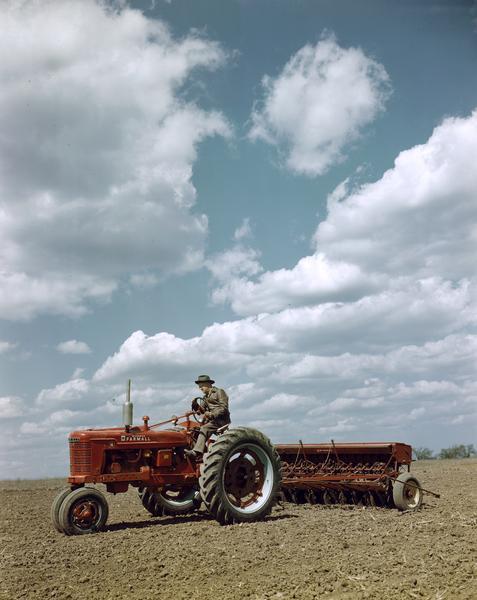 View of a man in a field operating a McCormick Farmall H tractor with attached grain drill, either at or near the company's experimental farm in Hinsdale.