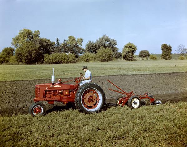 View towards the left side of a man on a McCormick Farmall tractor H pulling a plow, either at or near the company's experimental farm in Hinsdale.