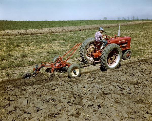 Man plowing a field with a McCormick Farmall H tractor and McCormick plow, at or near the company's experimental farm in Hinsdale, Illinois.