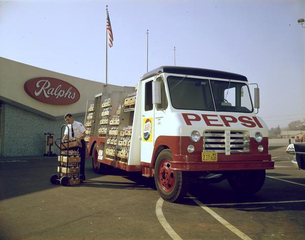 Color photograph of a delivery man unloading cases of bottled Pepsi (soda) from an International Metro truck in front of Ralph's Supermarket.