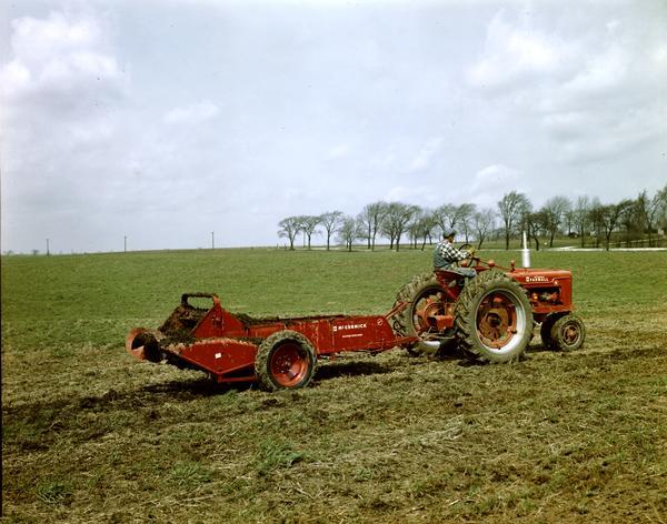 Slightly elevated view of a man pulling a McCormick No. 200 manure spreader with a  McCormick Farmall H tractor. Photograph was taken at or near the company's experimental farm at Hinsdale, Illinois.