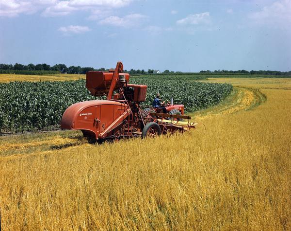 View across field of a man harvesting wheat with a Farmall M tractor and No. 122 combine (harvester-thresher).