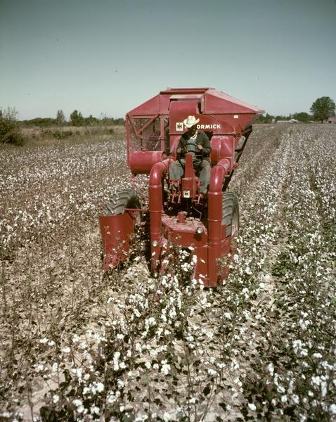 Man operating a 34HM-120 cotton picker mounted on a Farmall 400 tractor in a cotton field.