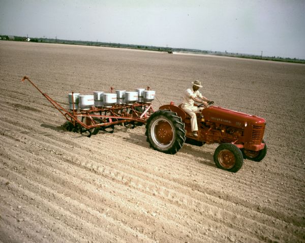 Color photograph of a man operating an International 309 utility tractor and planter.
