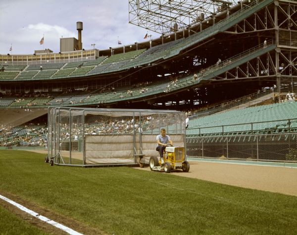 Color photograph of a man pulling a batting cage with a Cub Cadet lawn tractor at Metropolitan Stadium, home of the Minnesota Twins and Minnesota Vikings.
