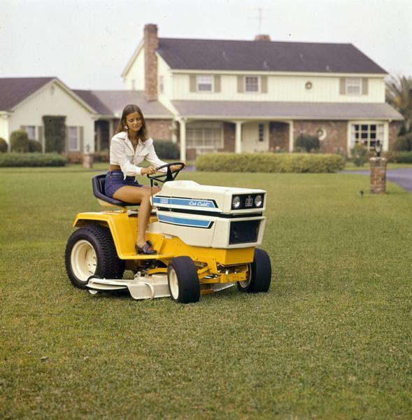 Color advertising photograph of a woman cutting grass outside a suburban home on a 1650 Cub Cadet lawn tractor.