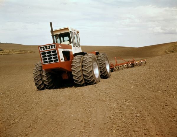 Color photograph of a man pulling a spring-tooth harrow through a field with an International 4366 turbo tractor.