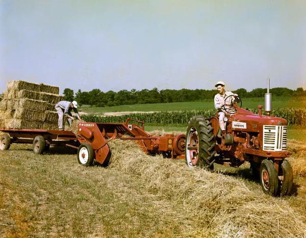 Two men baling hay with a Farmall tractor and McCormick hay baler.