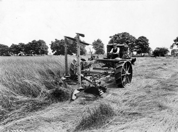 Three-quarter view from left front of a man operating an experimental motor-driven mower with two vertical lift sickle bars.
