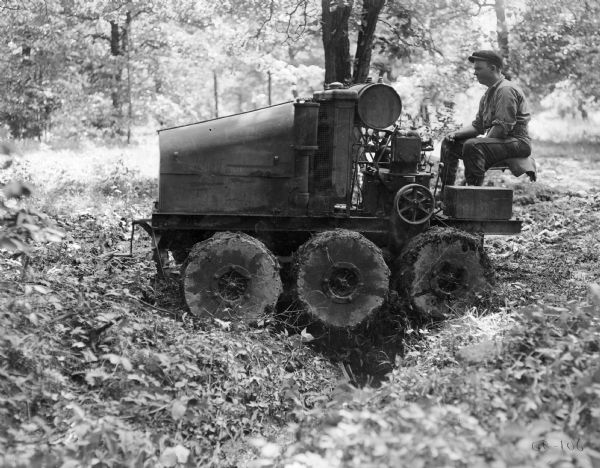 Man operating an experimental 8-16(?) tractor with six wheels over rough terrain.