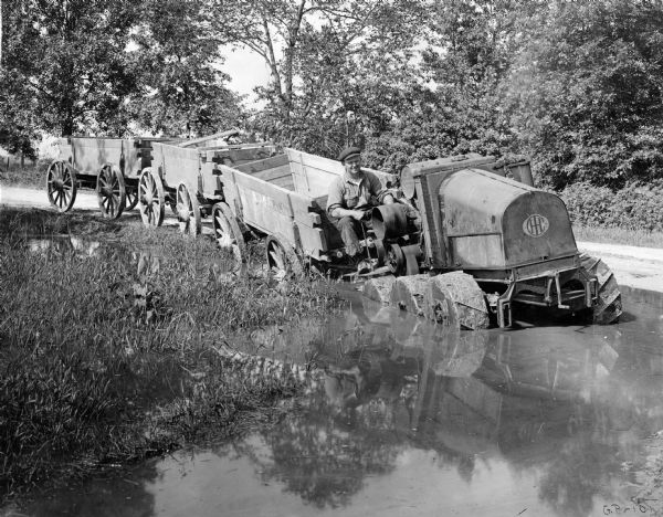 Man pulling wagons through water with an experimental 8-16(?) tractor with six wheels.