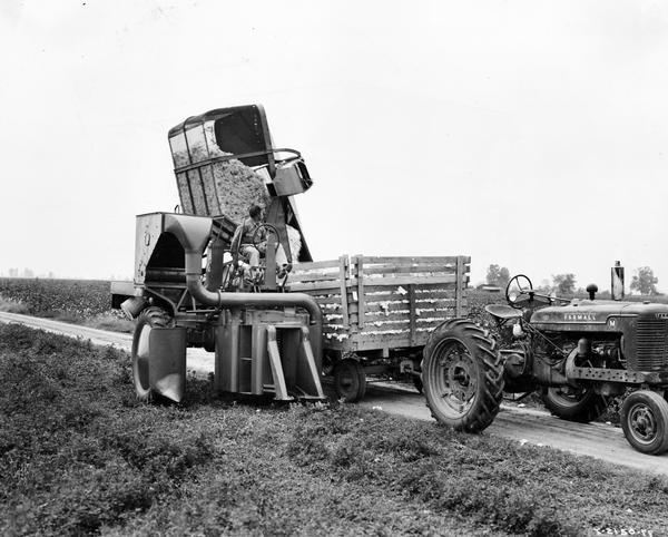 Farm worker dumping cotton from an International Harvester cotton picker into a trailer pulled by a Farmall M tractor.