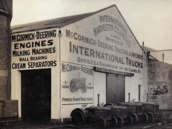Tractors parked in front of a dealership or warehouse building advertising International trucks and McCormick-Deering tractors and implements. The building was located in Christchurch, New Zealand and was owned by International Harvester Company of New Zealand.