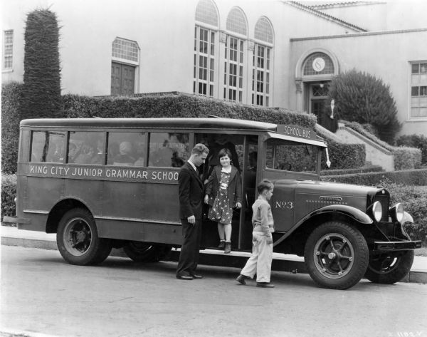 Children getting off of an International school bus for the King City Junior Grammar School as the bus driver stands by.