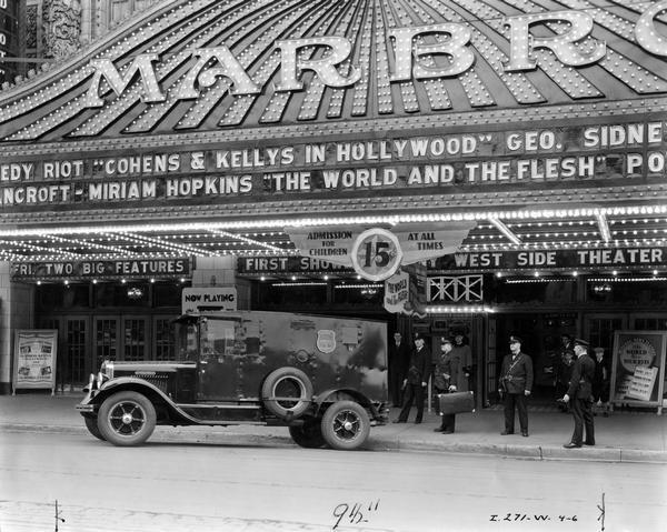 Armed guards loading a case of money(?) onto an International A-3 armor plated truck owned by the Brinks Express Company. The truck is parked outside the Marbro Theater in Chicago. The theater's marquee advertises "Cohens & Kellys in Hollywood" and "The World and the Flesh".