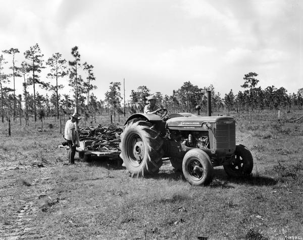 Farmers using a McCormick-Deering WR-9 tractor to haul a trailer loaded with timber. The words "rice field special" are on the tractor.