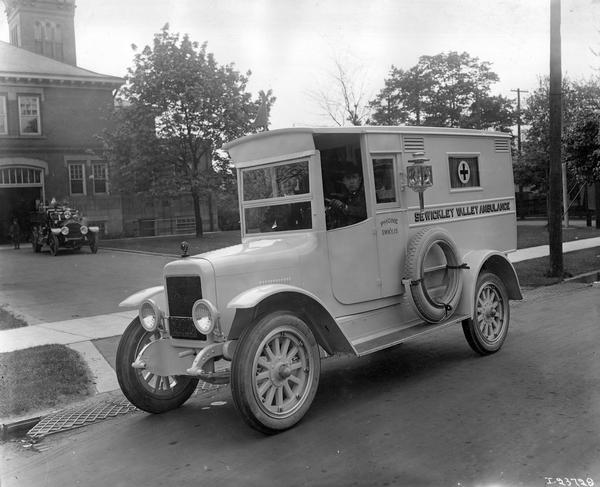 Sewickley Valley ambulance parked on a street outside a fire house or municipal building, with a fire truck parked near the garage door. The ambulance was built by International Harvester.