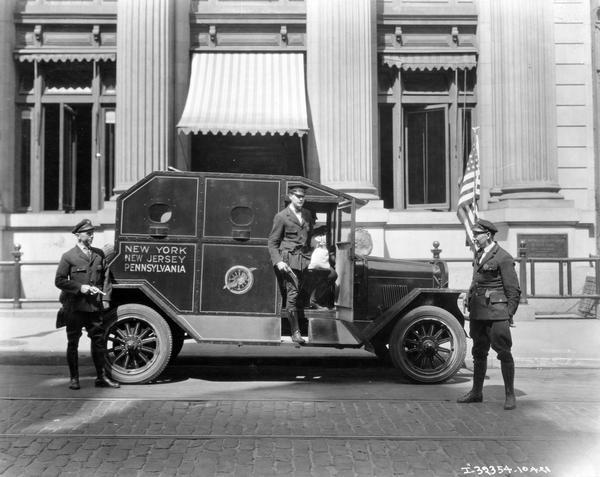 International armored bus parked outside the National City Bank of New York. Armed guards stand on either side of the truck and one is stepping out holding a sack.