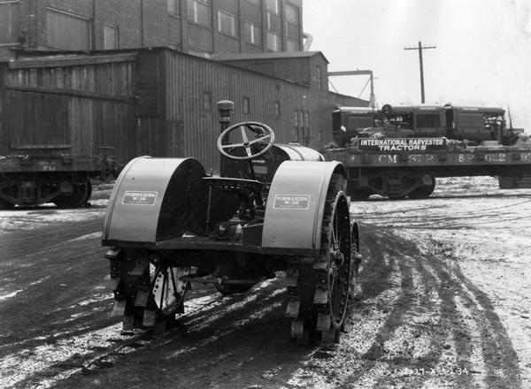 McCormick-Deering W-30 tractor outside a factory. A railroad flat car loaded with tractors is in the background.