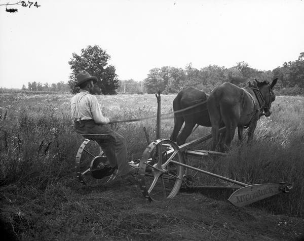 Farmer in a field using a McCormick mower drawn by two mules.