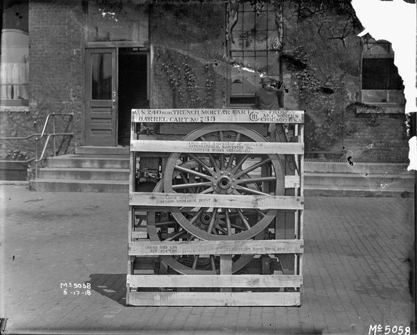Boxed 240 mm mortar cart ready for shipment to the U.S. military from International Harvester's McCormick Works. Includes a trench mortar barrel. A man is standing with his back turned at one of the factory windows.