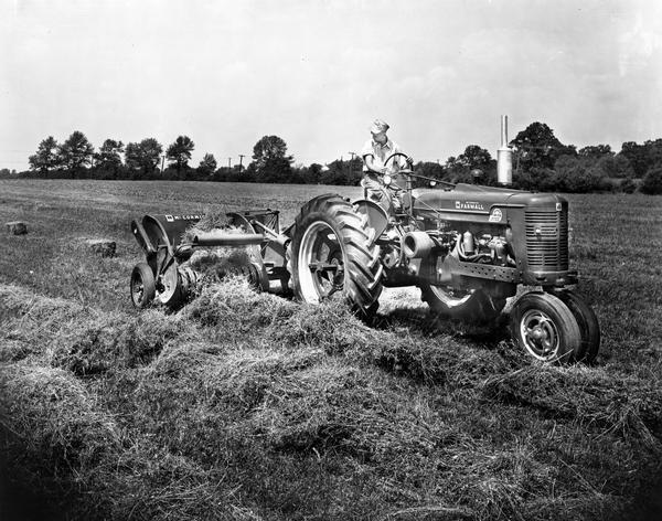 Farmer at work in field with McCormick Farmall Super M-TA tractor and baler.