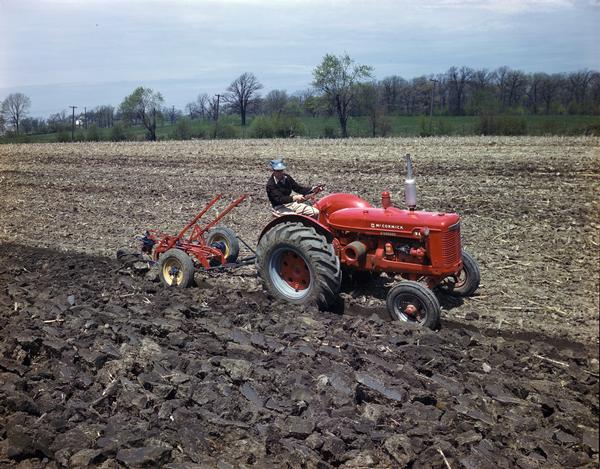 Right side view of a farmer plowing a field with a McCormick W-4 tractor and an attached moldboard plow.