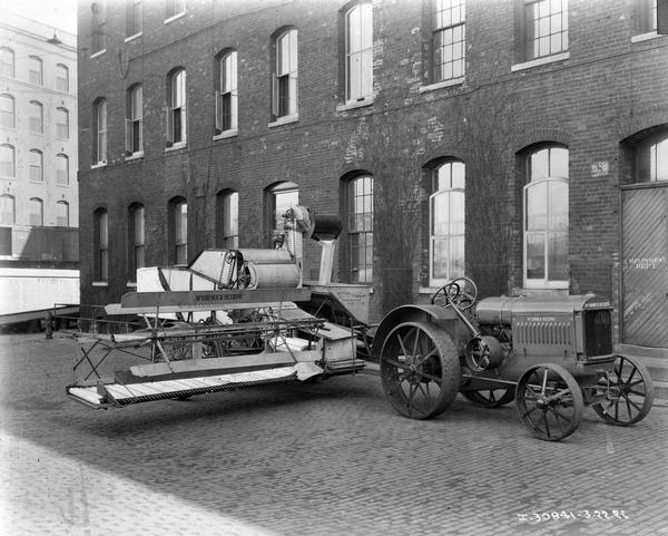 McCormick-Deering tractor and a No. 8 harvester-thresher (combine) parked in front of a factory building.