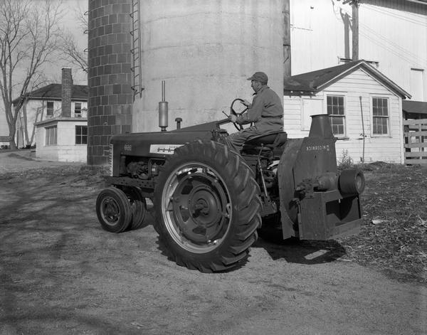 Farmer driving a McCormick Farmall 350 tractor with attached ensilage blower near a barn and silo.