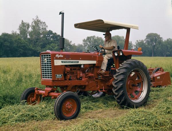 Left side view of a farmer operating an International Farmall 544 Hydro tractor in a field.