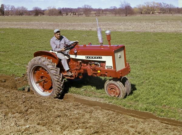 Slightly elevated view of a farmer plowing a field with a McCormick Farmall 404 tractor and an attached plow.