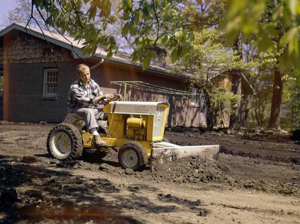 Color photograph of a man landscaping a yard with an International Cub Cadet tractor and attached blade.