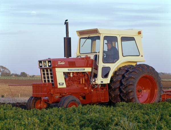 Color photograph of a farmer operating an International Farmall 1566 Turbo tractor in a field.