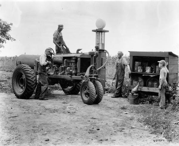 Men refueling and lubricating a Farmall tractor at a small service station on the farm of Tom Lanerty as a boy is looking on.
