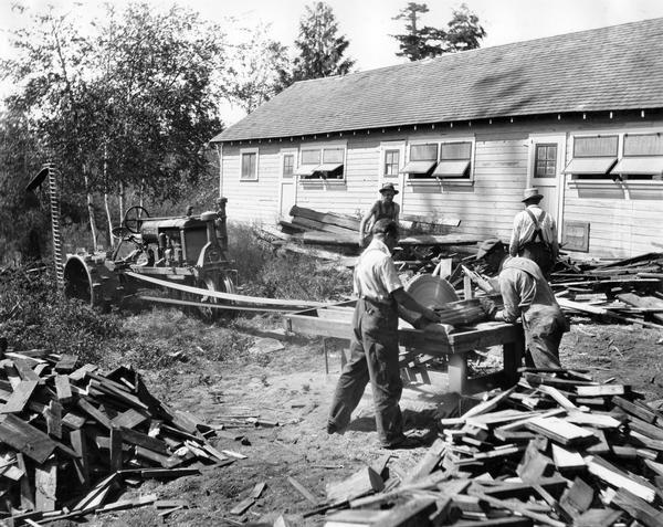 Men cutting firewood with a belt-driven saw powered by a McCormick-Deering Farmall F-30 tractor on the farm of Spencer Johnson.