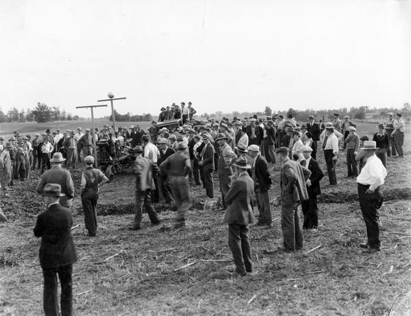 Crowd watching a demonstration of a radio-controlled McCormick-Deering Farmall F-30 tractor at an agricultural exhibition or fair.