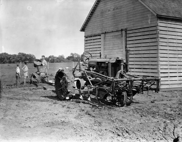 Farmer John Atkins grinding corn with a belt-driven feed grinder powered by a McCormick-Deering Farmall tractor. Mr. Atkins' son and daughter look on.