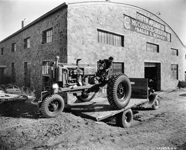 Man unloading a McCormick-Deering Farmall F-30 tractor from the bed of a truck in front of the Griffin Implement Company, an International Harvester dealership.