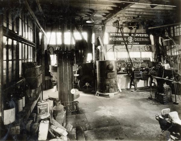 Interior a service shop at an International Harvester dealership owned by Dan Pullin and Son. The shop contains a coal furnace, tools, engines, belts, supplies and advertising signs.