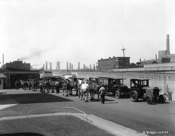 A line of horses are entering the McCormick Works (factory) gate as a line of trucks and a tractor are exiting. The tractor appears to be an industrial tractor with an enclosed cab adapted from a truck.