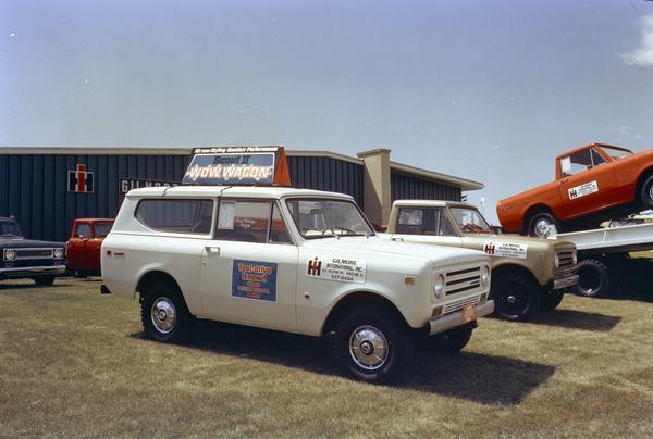 Color photograph of International Scout II pickup trucks parked on the lot of Gilmore International, Inc., an International Harvester dealership. The Scout in the foreground has a small advertising billboard mounted to its roof that reads: "Wow Wagon."
